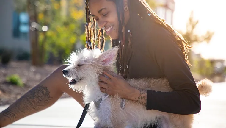 An androgynous African American person with there pet dog outdoors in a park.