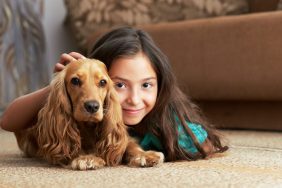 Young girl resting on carpet with Cocker Spaniel — one of the best dogs for kids and children.