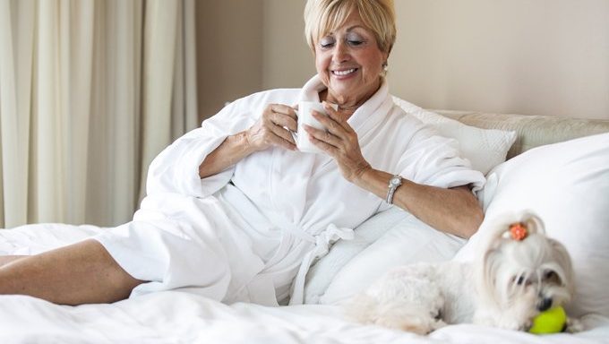 woman in robe on hotel bed with dog