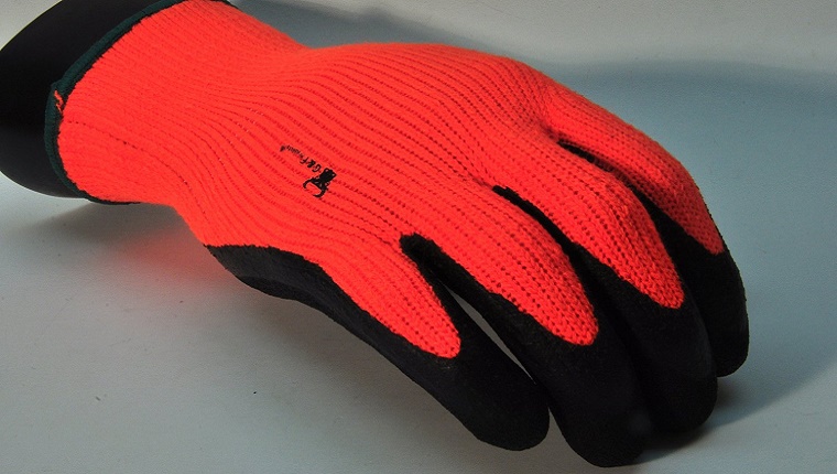 An orange glove with black gripping material on the fingers is displayed on a grey background.