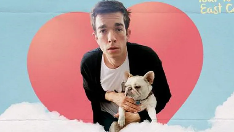 John Mulaney holds his white French Bulldog in front of a heart-shaped graphic.
