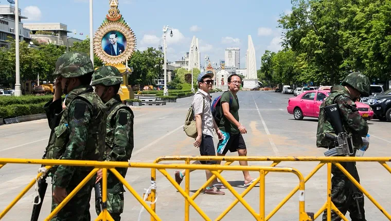 Military personnel stand next to a gate on a Thai street with an image of the king in the background.