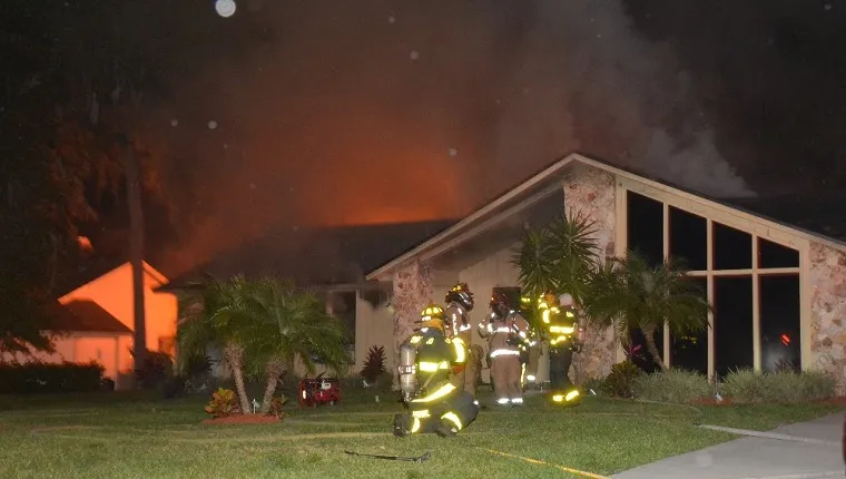 Firefighters stand outside the burning house.