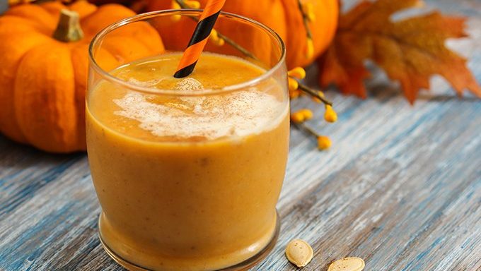 pumpkin smoothie with straw in front of fall decorations