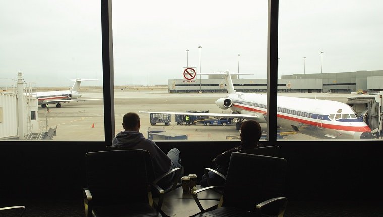 Silhouette of people watching thru an airport window. Parked planes and airport.