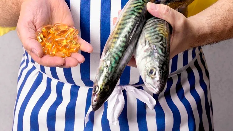 Fishmonger holding mackerel and Cod Liver oil tablets, close-up, mid section