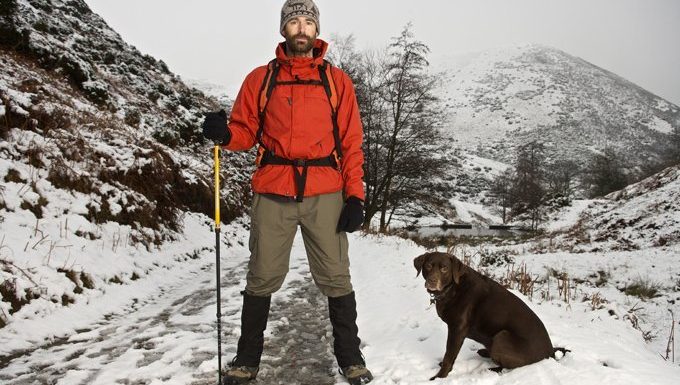 man and dog hiking in snowy mountains