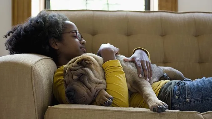young girl cuddling shar pei on couch