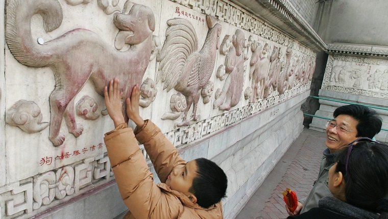 BEIJING, CHINA: A child rubs his hands for good luck on a bas-relief sculpture of a dog along a wall depicting the twelve animals of the lunar calendar, 27 January 2006, at the White Cloud Taoist Temple (Baiyun Guan) in Beijing. Founded in A.D 739, the White Cloud Temple is one of the oldest Taoist temples in northern China and attracts thousands of visitors for its temple fair during the Spring Festival holidays to celebrate the Lunar New Year, which falls on 29 January with the Year of the Dog. AFP PHOTO/Frederic J. BROWN (Photo credit should read FREDERIC J. BROWN/AFP/Getty Images)