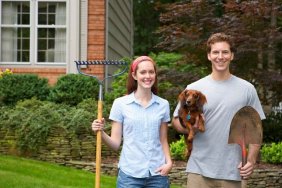 Young couple holding dog and garden tools