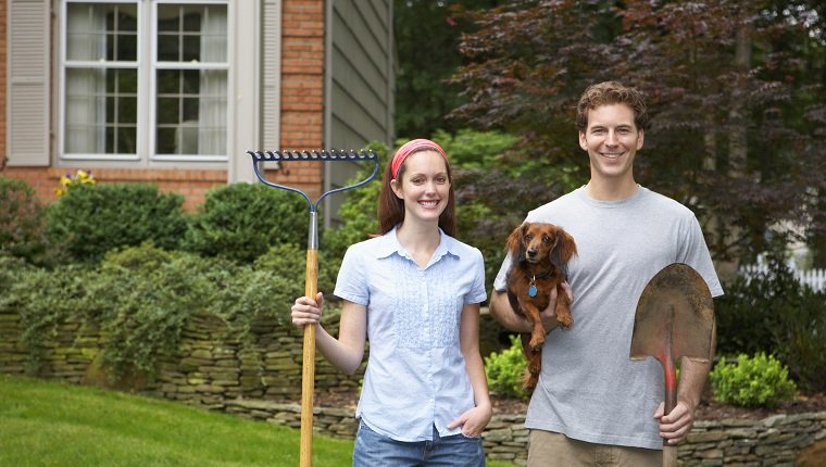 Young couple holding dog and garden tools