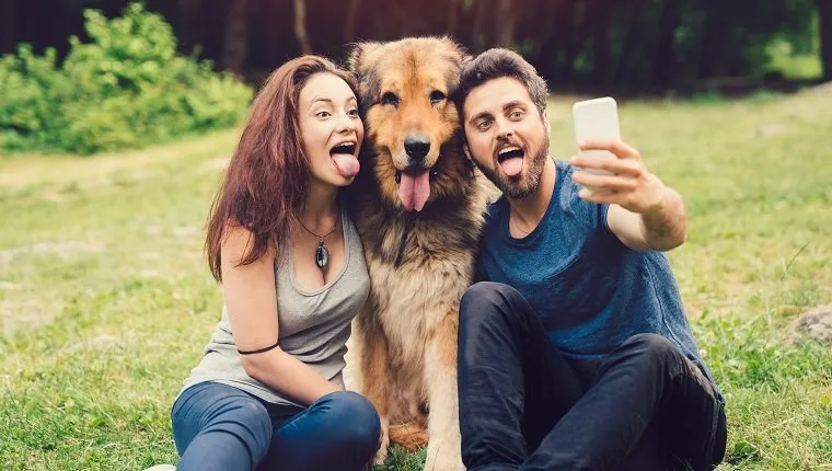 Young couple and dog sticking out tongues for a selfie at the countryside