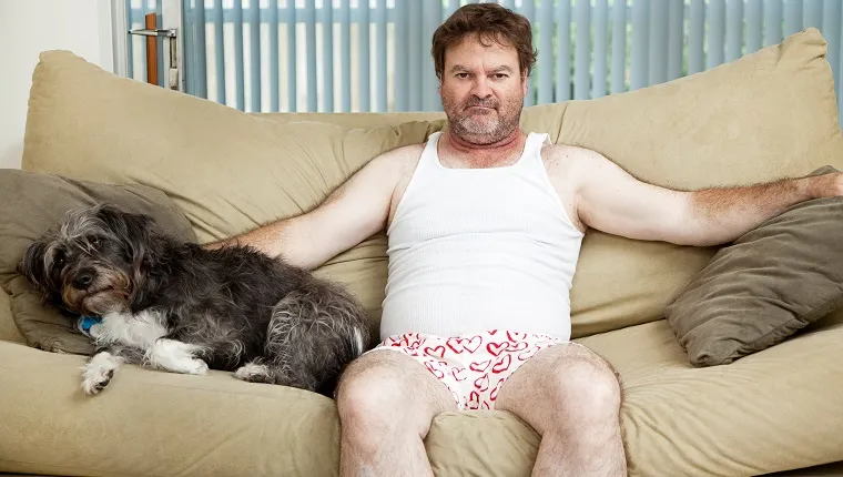 Discouraged unemployed man at home in his underwear, sitting on the couch with his dog.