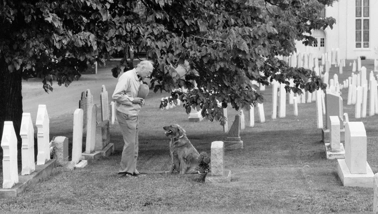 ELDERLY MAN HAT OVER HIS HEART AND PET DOG VISITING GRAVE OF LOVED ONE IN CHURCHYARD CEMETERY (Photo by Camerique/ClassicStock/Getty Images)