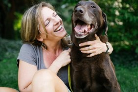 Smiling woman sitting on grass with Labrador Retriever
