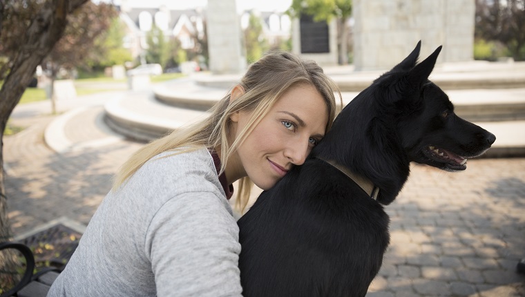 Affectionate female pet owner hugging black dog in park