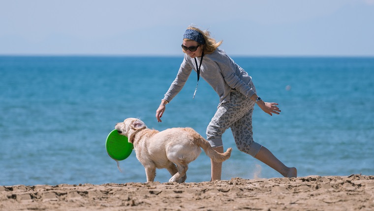 Happy women playing with her dog at the beach.