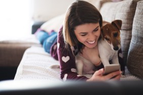 Beautiful woman using a mobile phone while lying with her dog.