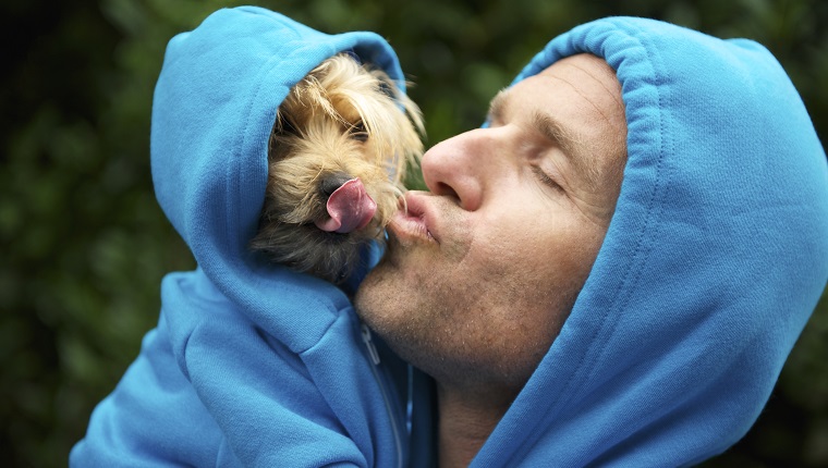 Man kisses his best friend dog in matching blue hoodies in bright green park background outdoors