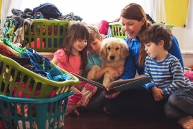 Smiling mother reading to three children and golden retriever puppy dog surrounded by laundry baskets