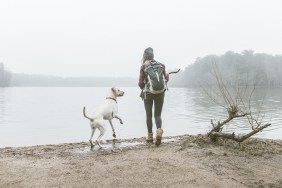Young woman throwing stick for her dog on misty lakeside