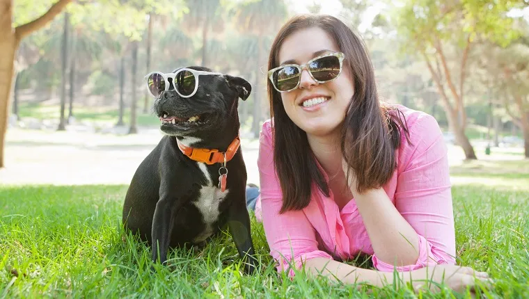 Portrait of young woman and dog lying in park wearing sunglasses