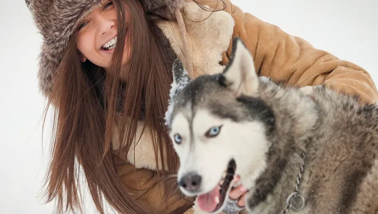 Portrait of happy woman with Siberian Husky during winter