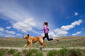 A female and her yellow lab jogging down a deserted dirt road.