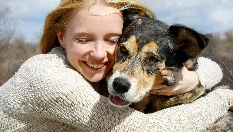 a loving and candid portrait of a happy woman hugging her large German Shepherd dog.