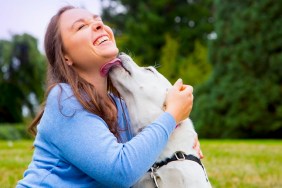 Young woman sitting with dog in park, dog licking womans face
