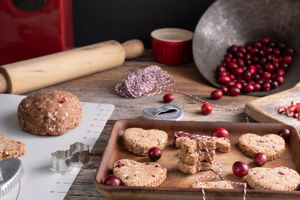 Biscuits et friandises à base de canneberges que les chiens peuvent manger en toute sécurité, disposés à côté d'un rouleau à pâtisserie et d'une surface de cuisson.