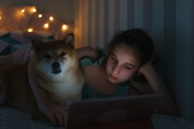 Close up view of a girl lying on her bed watching a sad dog movie next to her Shiba Inu on her digital tablet inside the bedroom.