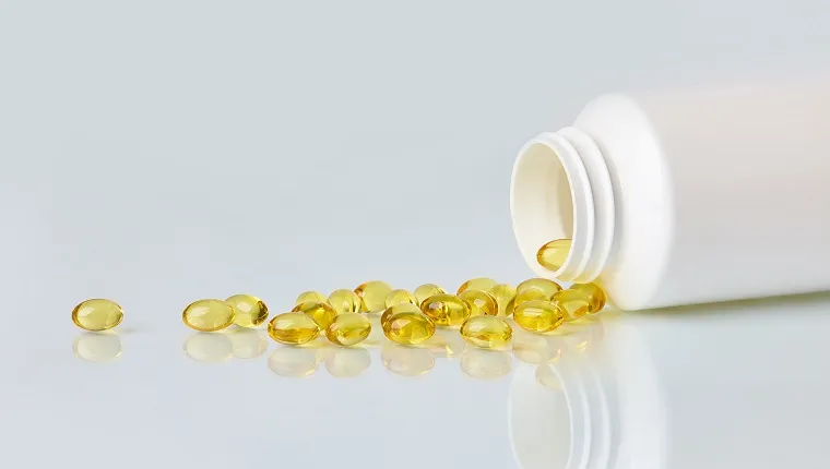 Fish oil capsules scattered from white plastic bottle on white background.  Health care concept.