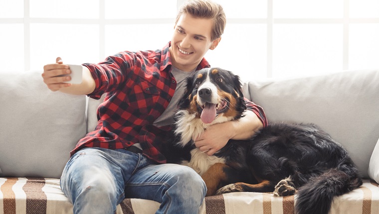 Young man with dog at home taking photos