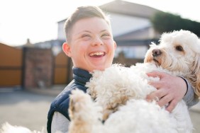 A boy with down syndrome hugs his pet dog in the driveway.