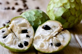 closeup of some custard apples, one of them cut in half, on a rustic wooden surface