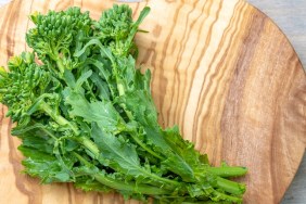 Fresh uncooked rapini vegetable over a heart-shape cutting board