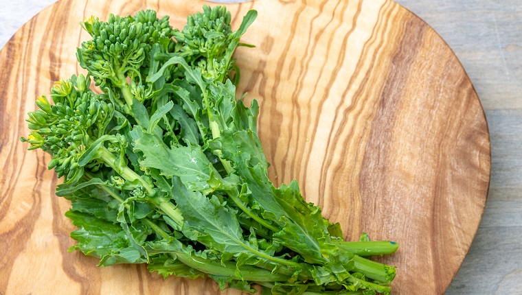 Fresh uncooked rapini vegetable over a heart-shape cutting board