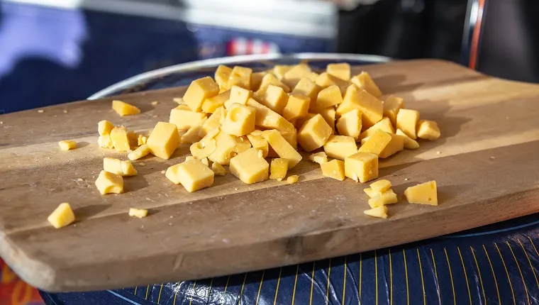 many small pieces of sliced cheese on a wooden board on top of a round cheese wrapped in blue