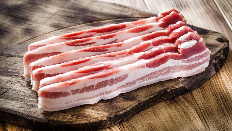 Sliced pancetta on a cutting board shot on wooden kitchen table. DSRL studio photo taken with Canon EOS 5D Mk II and Canon EF 100mm f/2.8L Macro IS USM