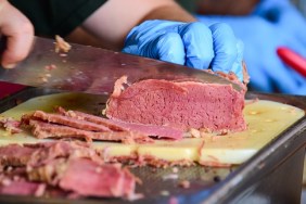 Close up of a hand wearing protective glove holding and slicing pastrami on a cutting board at a food market
