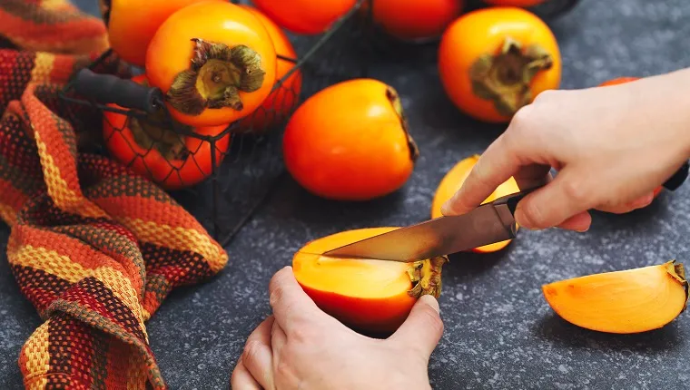 Woman's hands cutting fresh persimmon fruits.