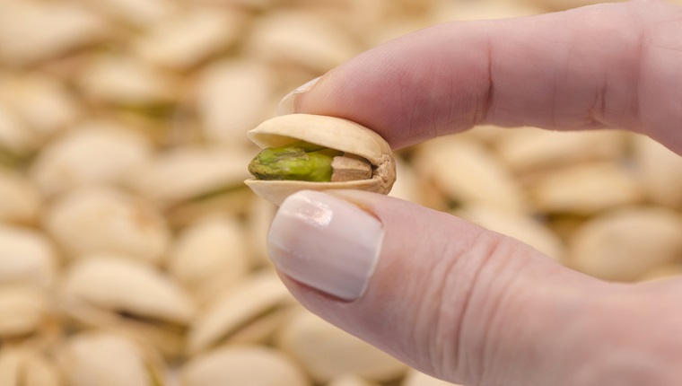 Woman's hand holding tasty pistachio, close up. Healthy eating.