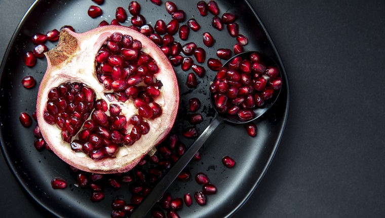 Pomegranate half placed on a plate with the seeds spread on plate.