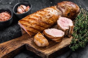 BBQ roasted pork tenderloin fillet meat on wooden board with herbs. Black background. Top view.