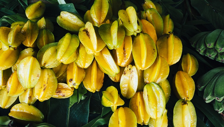 Close up of star fruits and green bananas for sale along the side of the road.