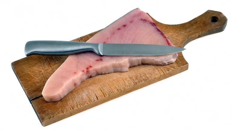Raw swordfish steak on a cutting board with a knife in close-up on a white background