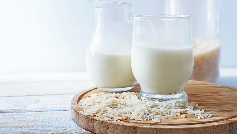 Vegan rice milk, healthy alternative without animal dairy products in a drinking glass and a jug on a wooden kitchen board against a light background, copy space, selected focus, narrow depth of field