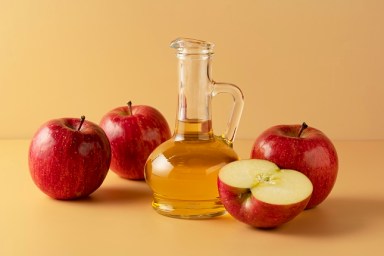 Apple vinegar in a glass container on a beige background with lots of apples around it."n