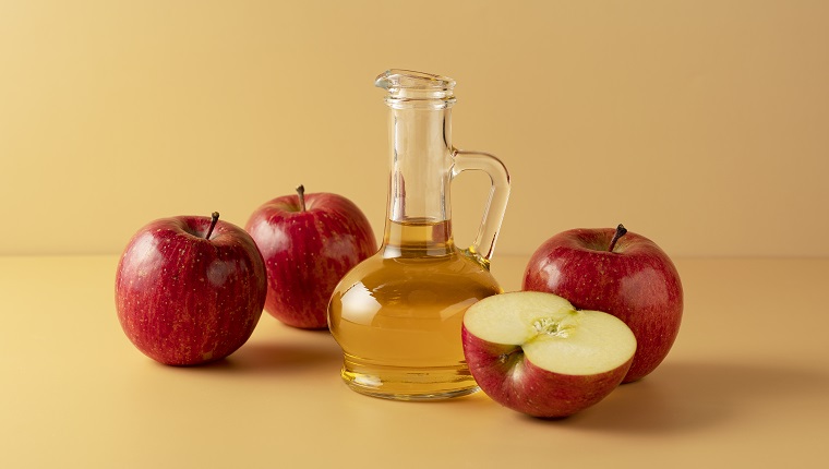 Apple vinegar in a glass container on a beige background with lots of apples around it."n